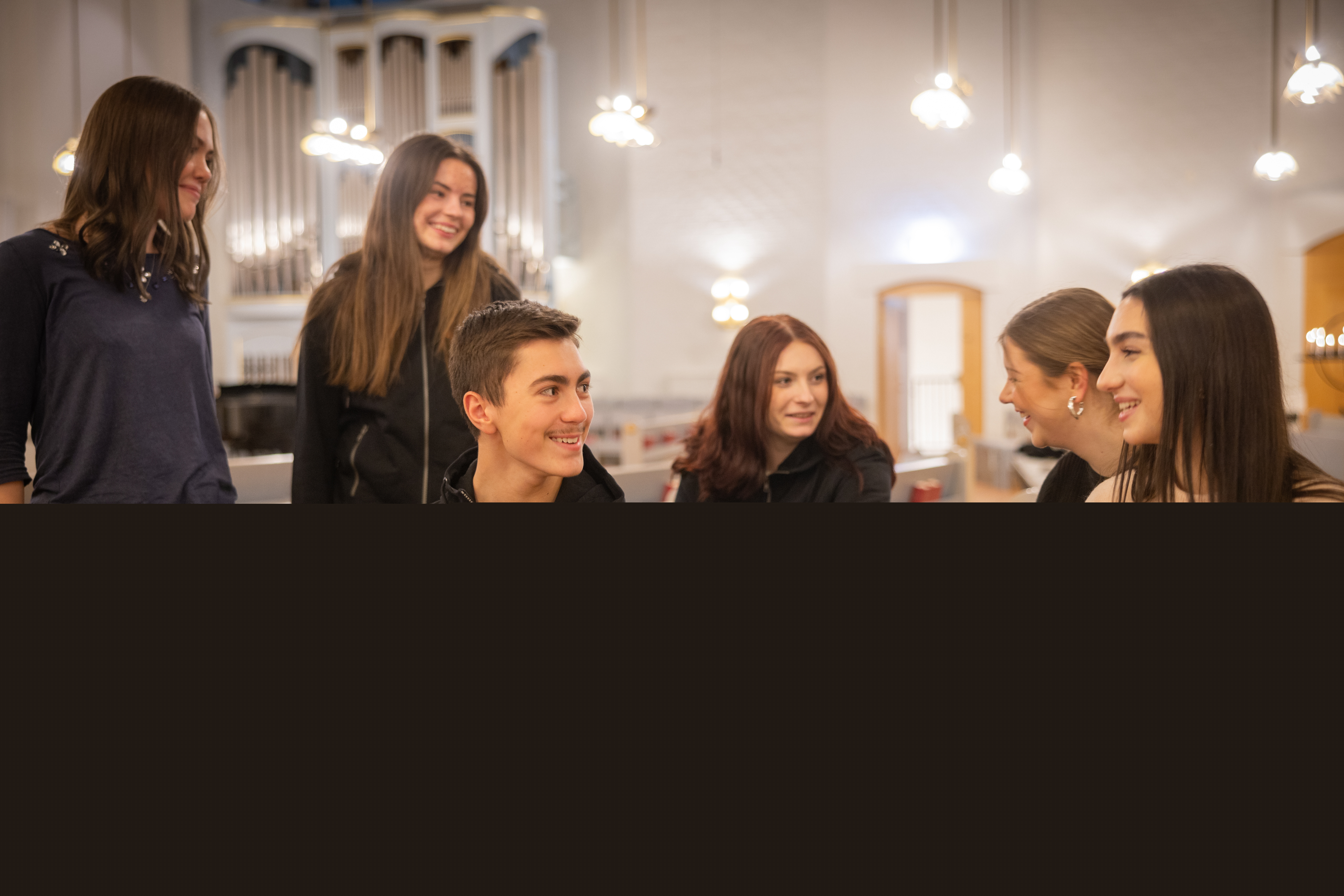 Flera ungdomar samtalar med varandra i en kyrka. Biblar utställda i bänkraderna.