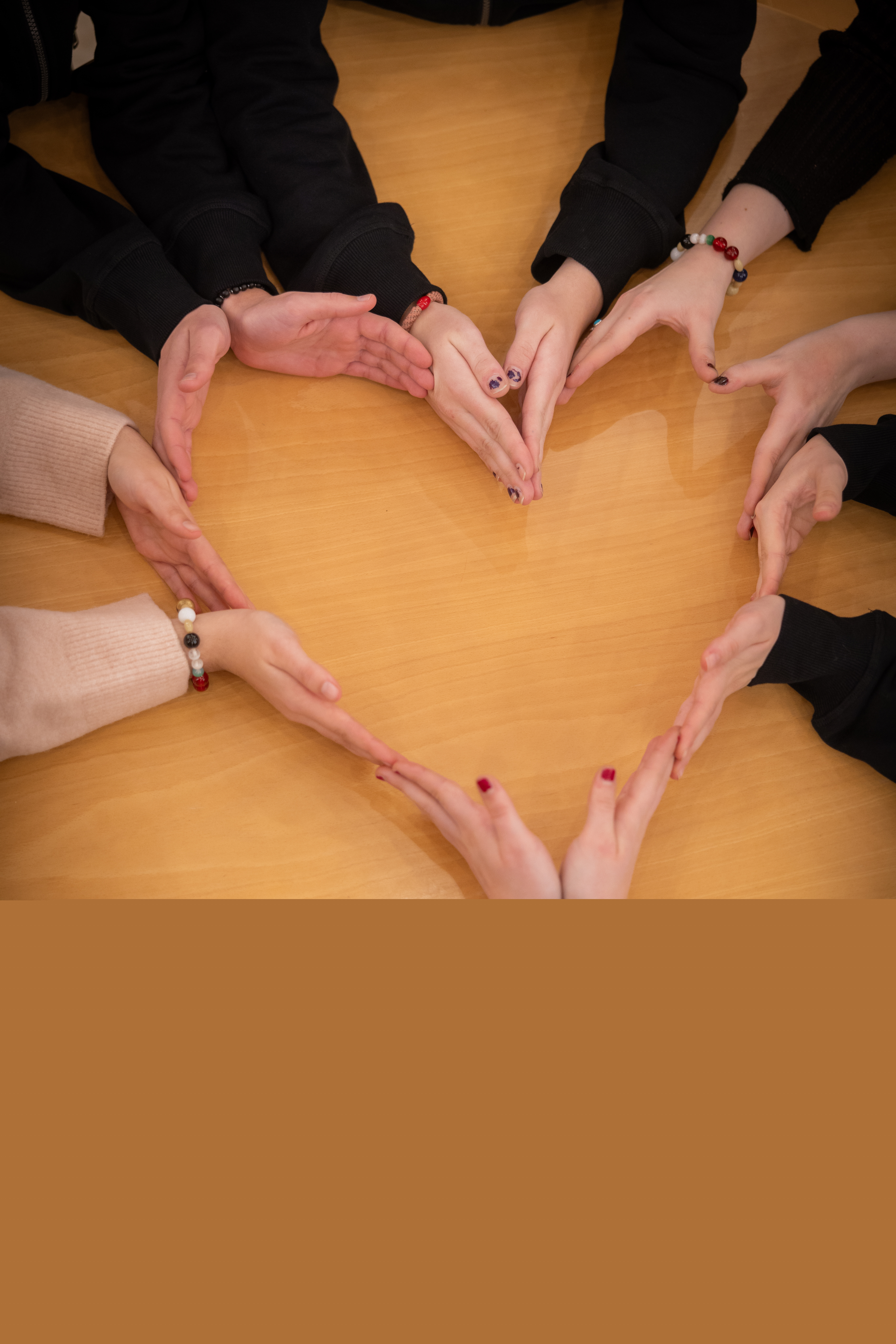 Flera personer sitter vid ett bord och formar  ett hjärta med hjälp av sina händer.