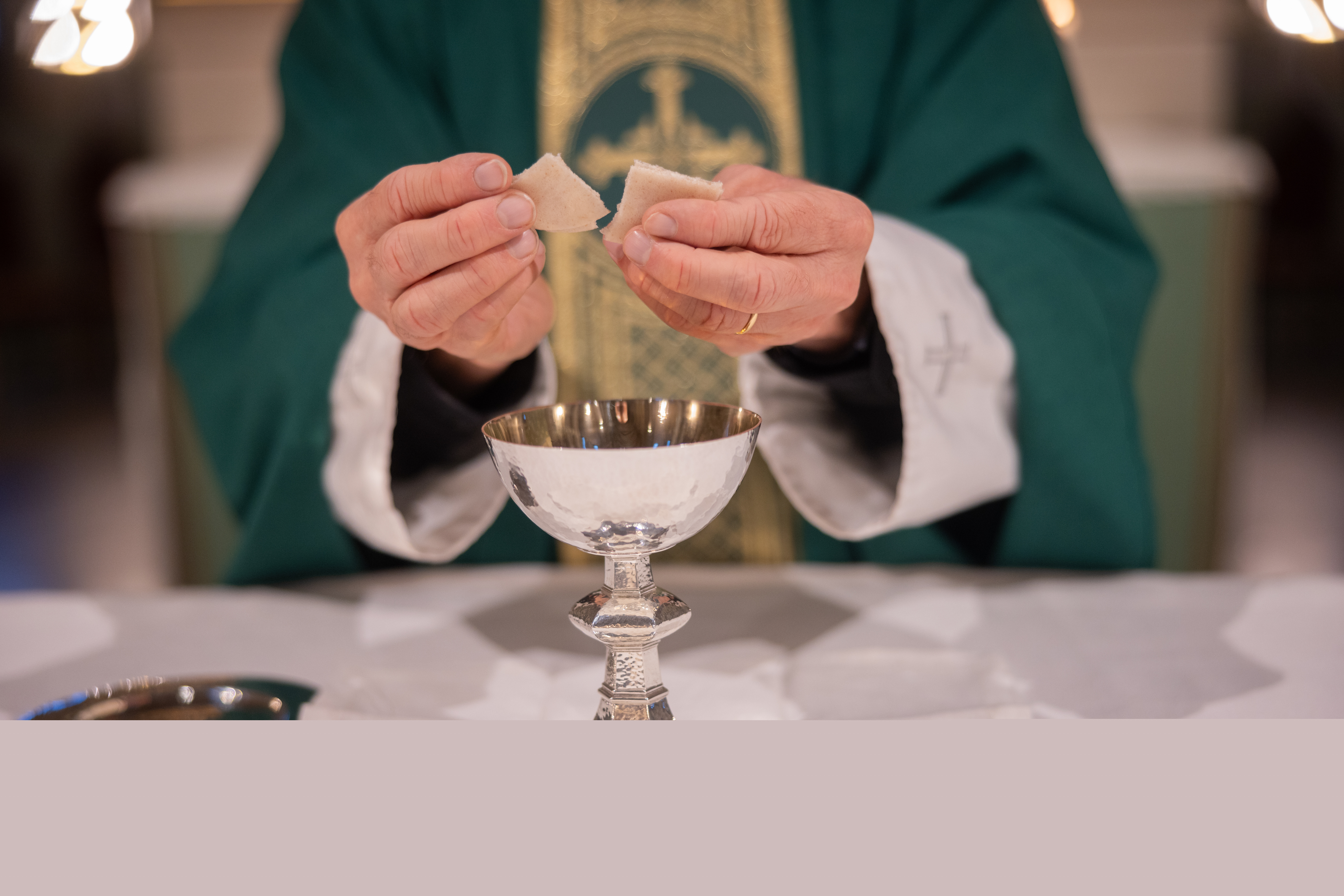 En präst bryter en oblat över nattvardskalken.