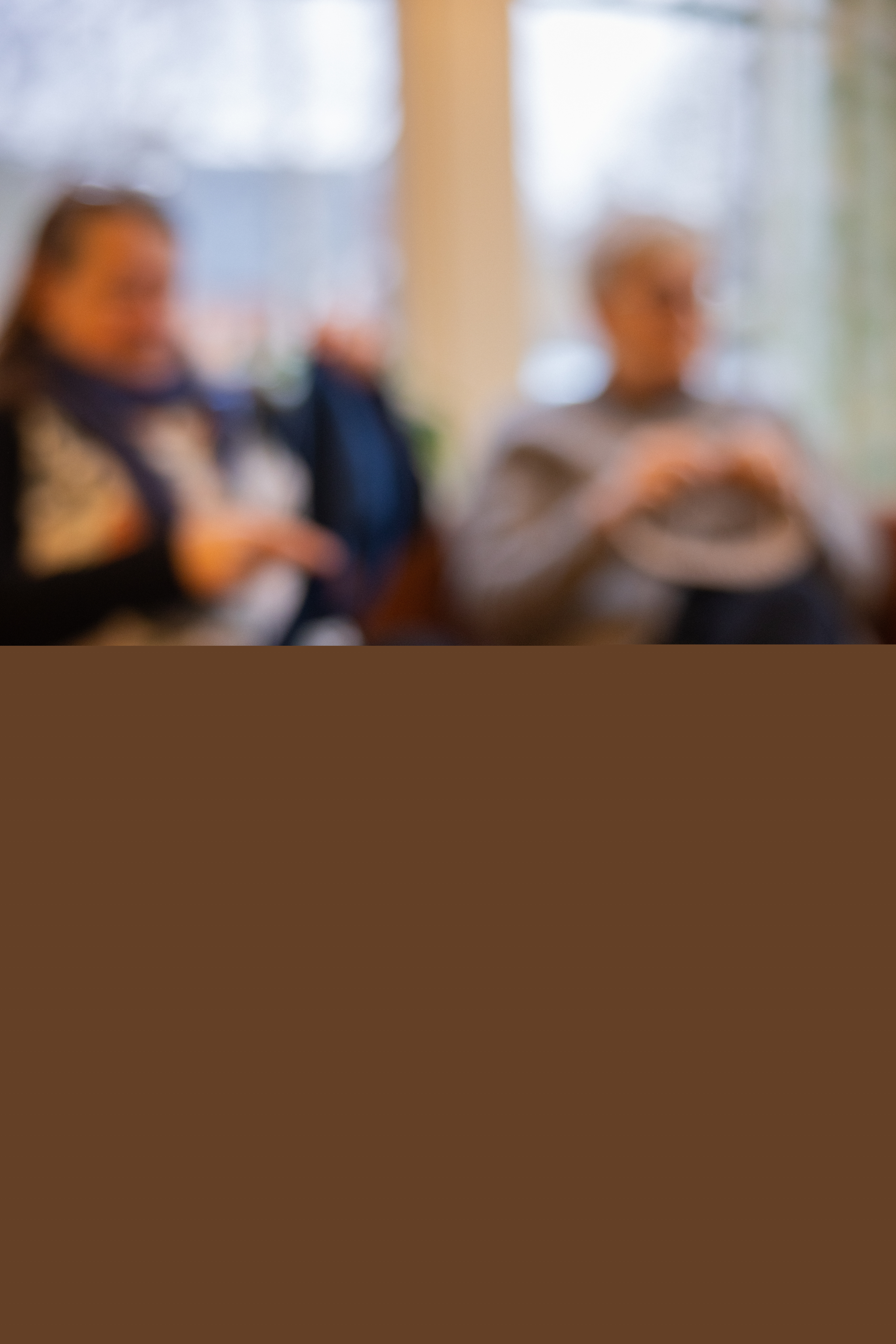 Närbild på garnnystan och två virkade små bin i en korg. Två personer stickar i bakgrunden.