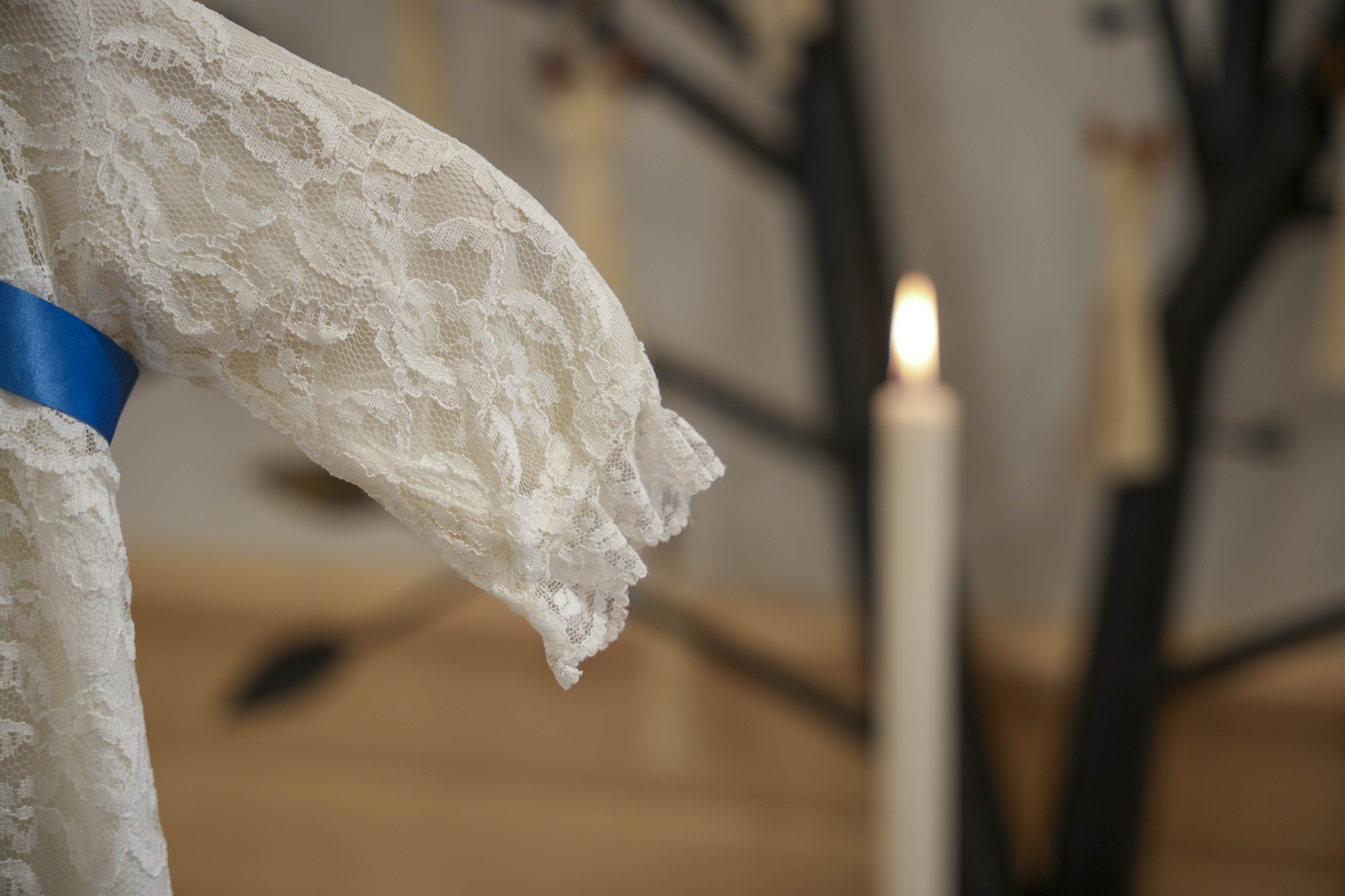 En dopklänning i vit spets med blått band. Ett stearinljus brinner i bakgrunden.
