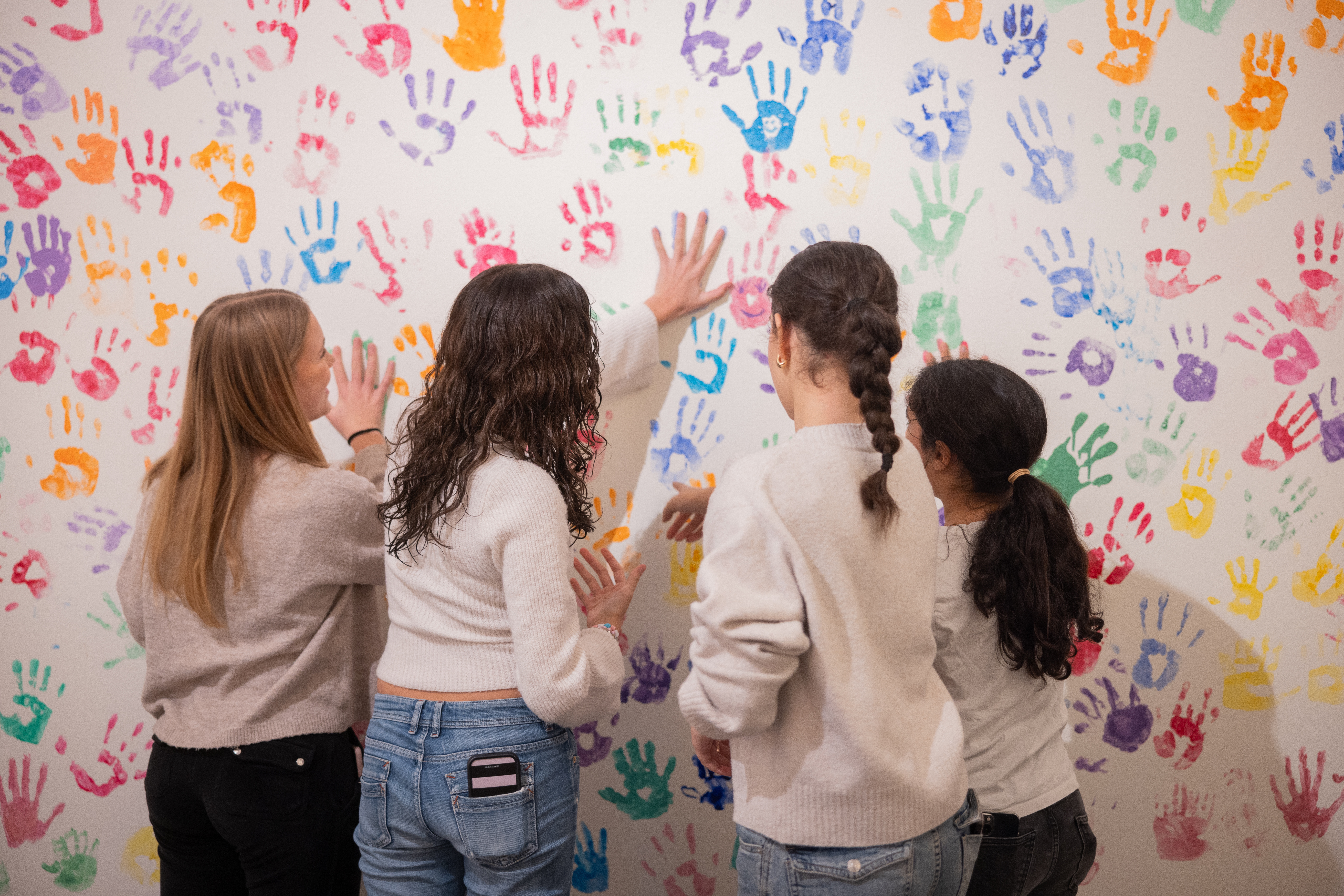 Fyra tjejer har färgat sina händer letar nu tomma ytor på en vägg full av färgglada handavtryck.