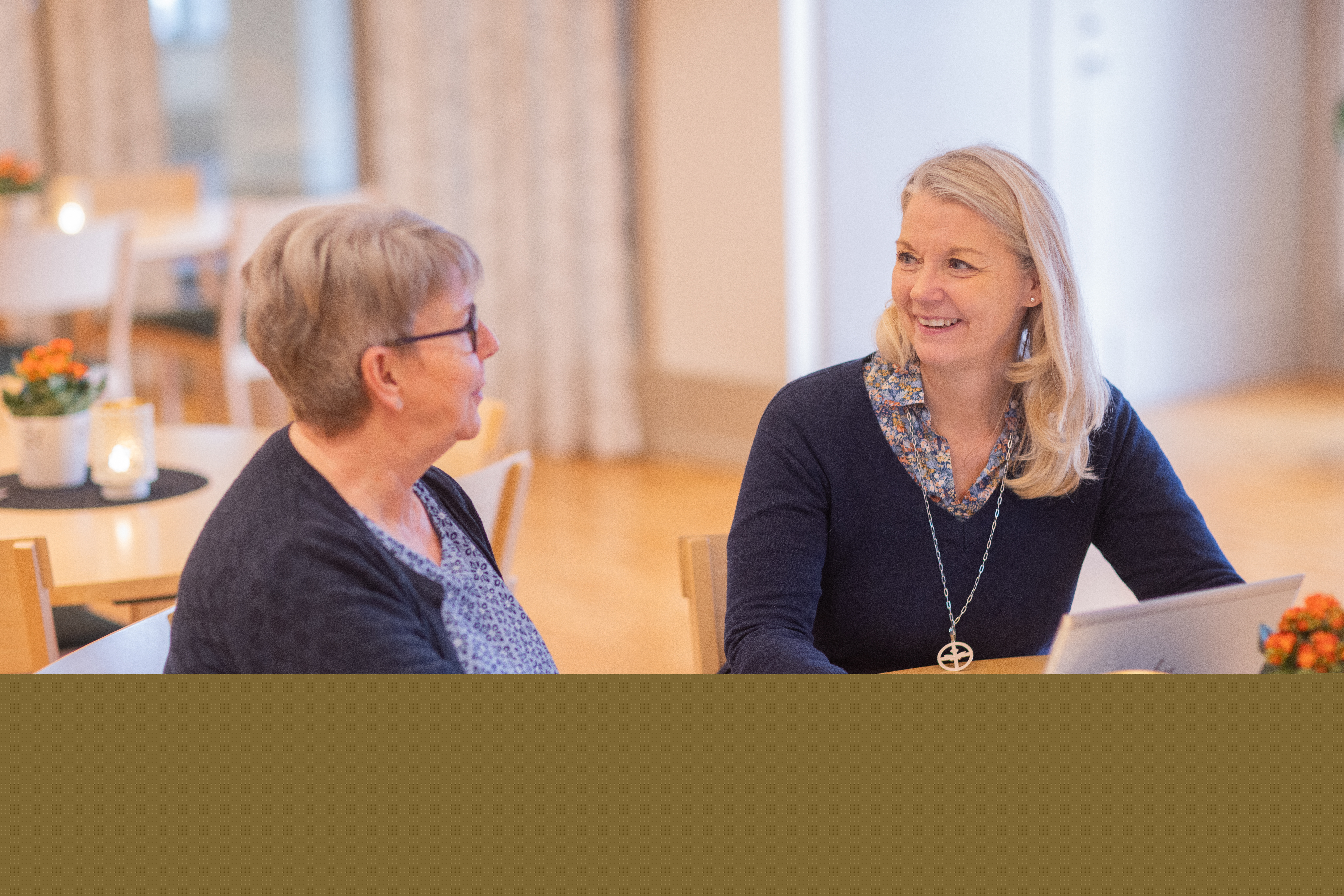 Två kvinnor som sitter vid ett bord har ett trevligt samtal framför en dator.