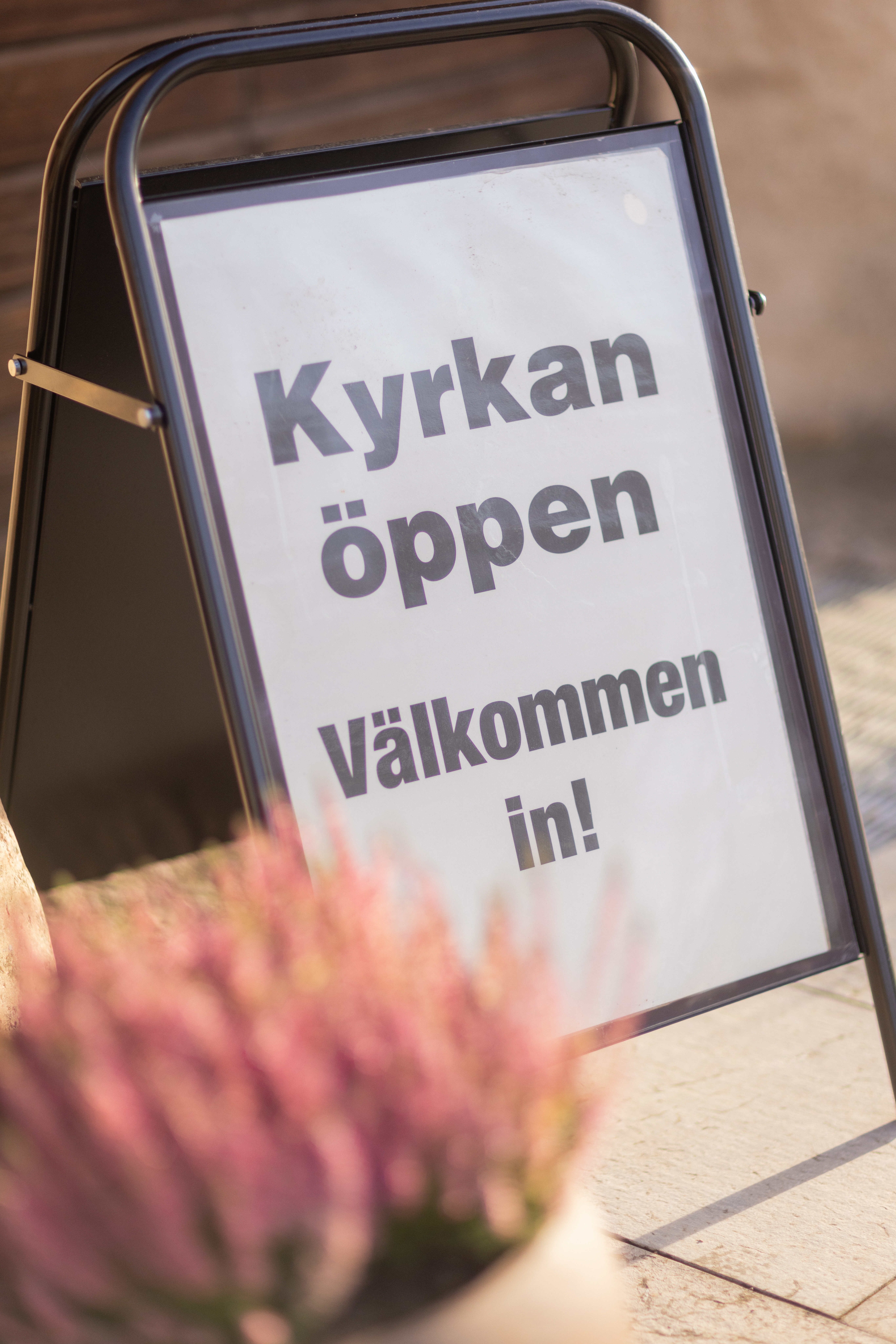 En trottoarpratare med texten Kyrkan öppen, välkommen in!
