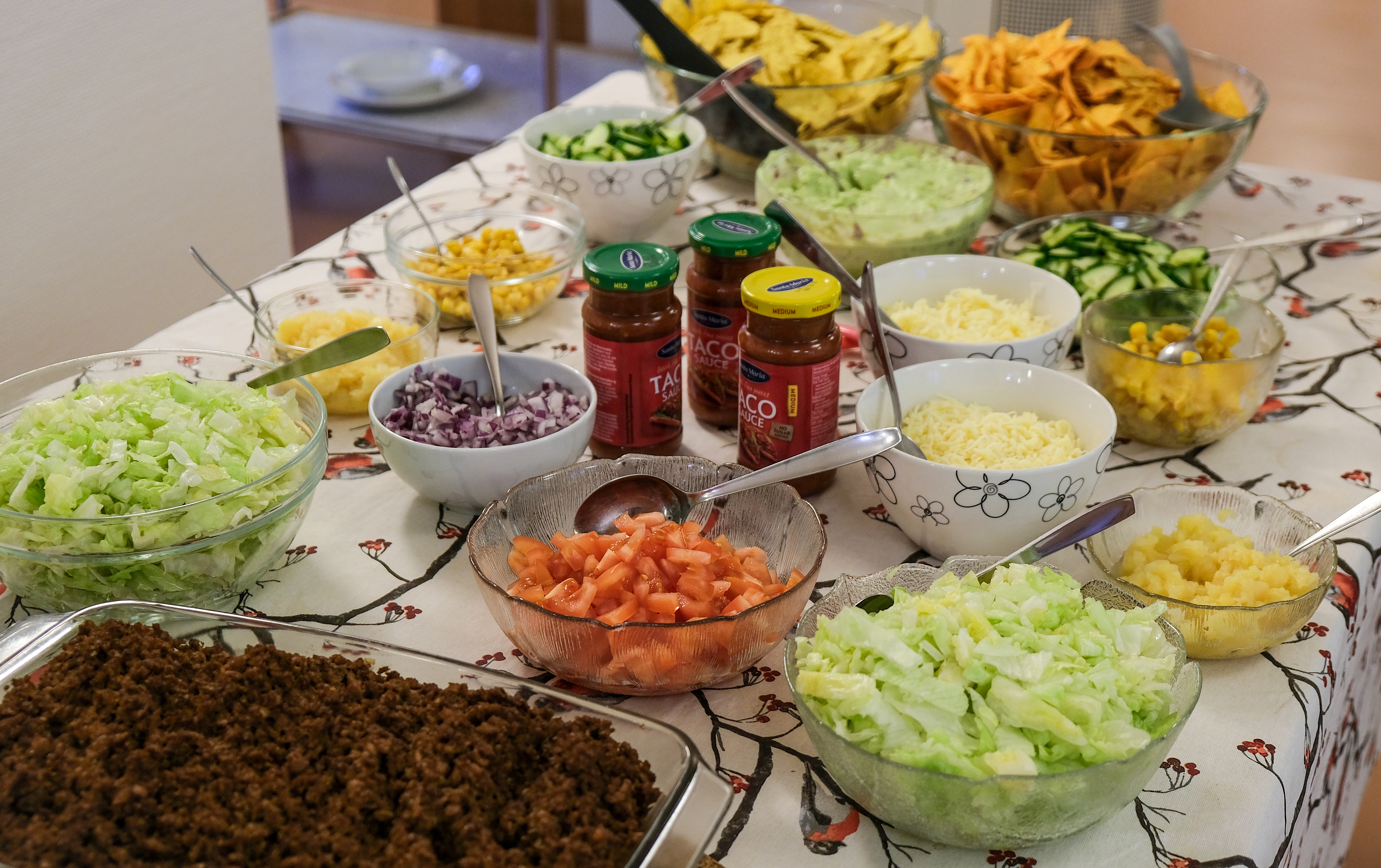 Köttfärs med olika grönsaker, ost m m uppdukade till en tacobuffé på ett bord.