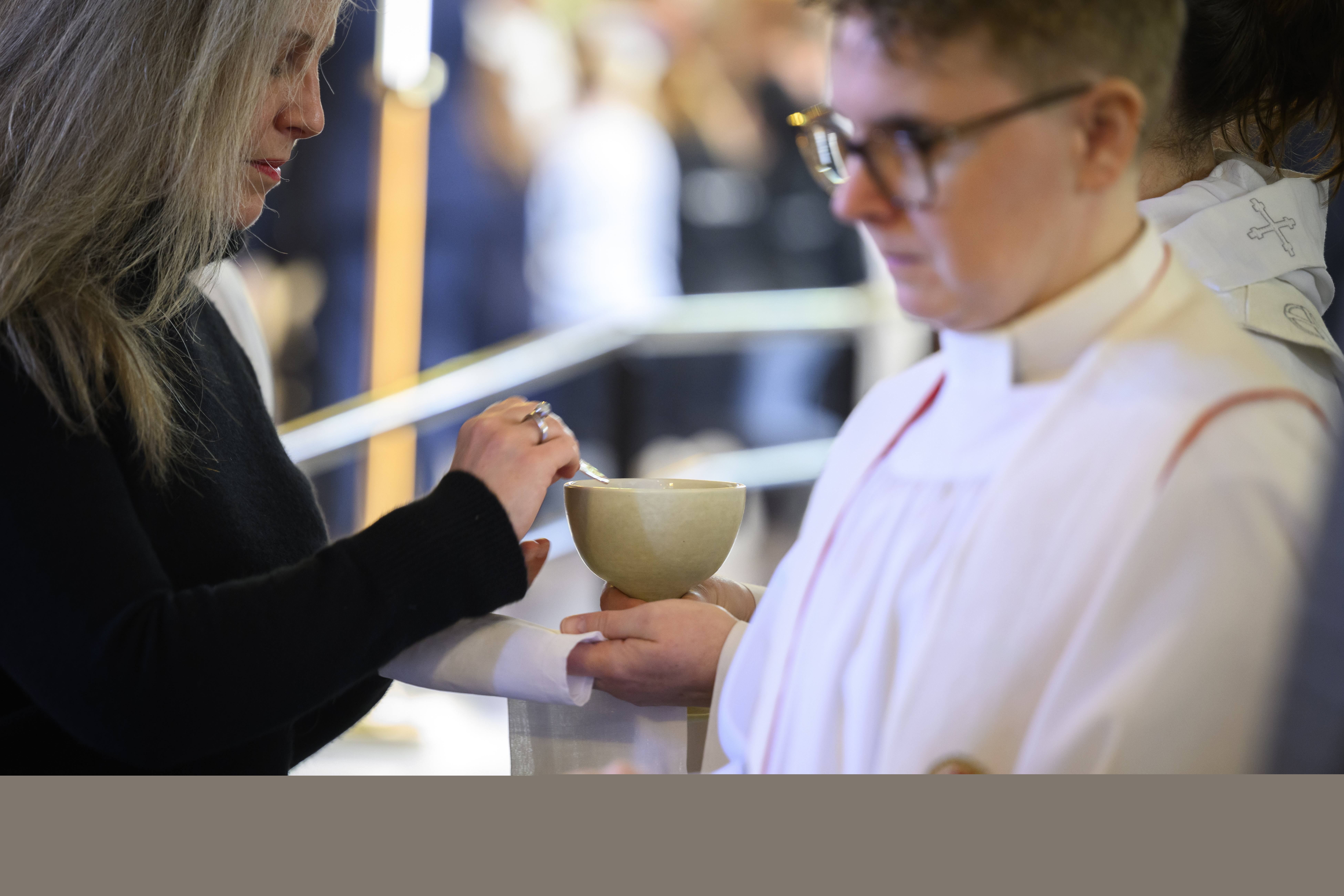 En kvinna i svarta kläder håller en oblat i sin ena hand. Prästen räcker fram kalken.