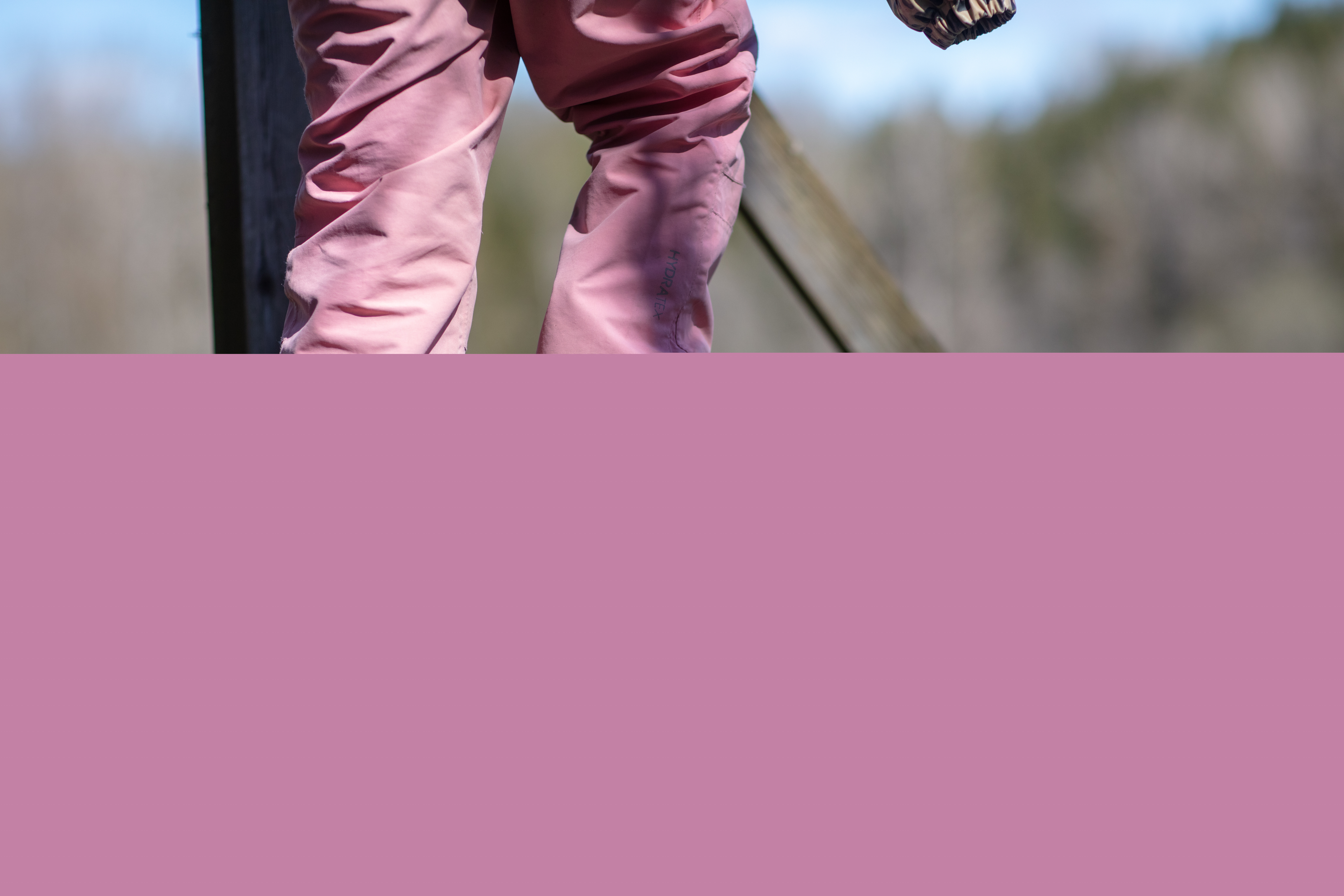 Ett barn i rosa täckbyxor och lila stövlar går över en trappassage vid ett naturreservat.