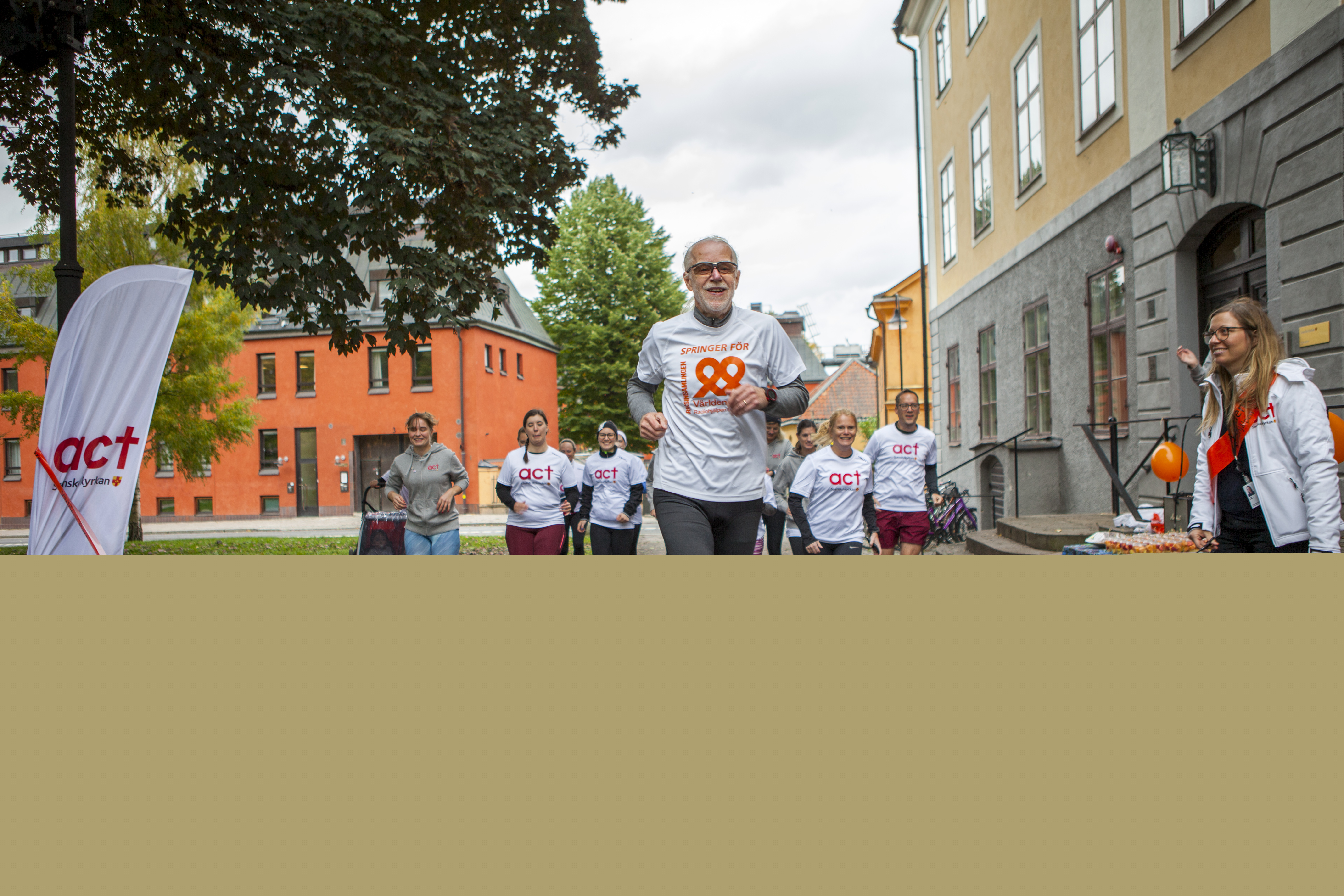 En grupp människor springer mot kameran. Det står Världens Barn eller Act Svenska kyrkan på deras kläder. 