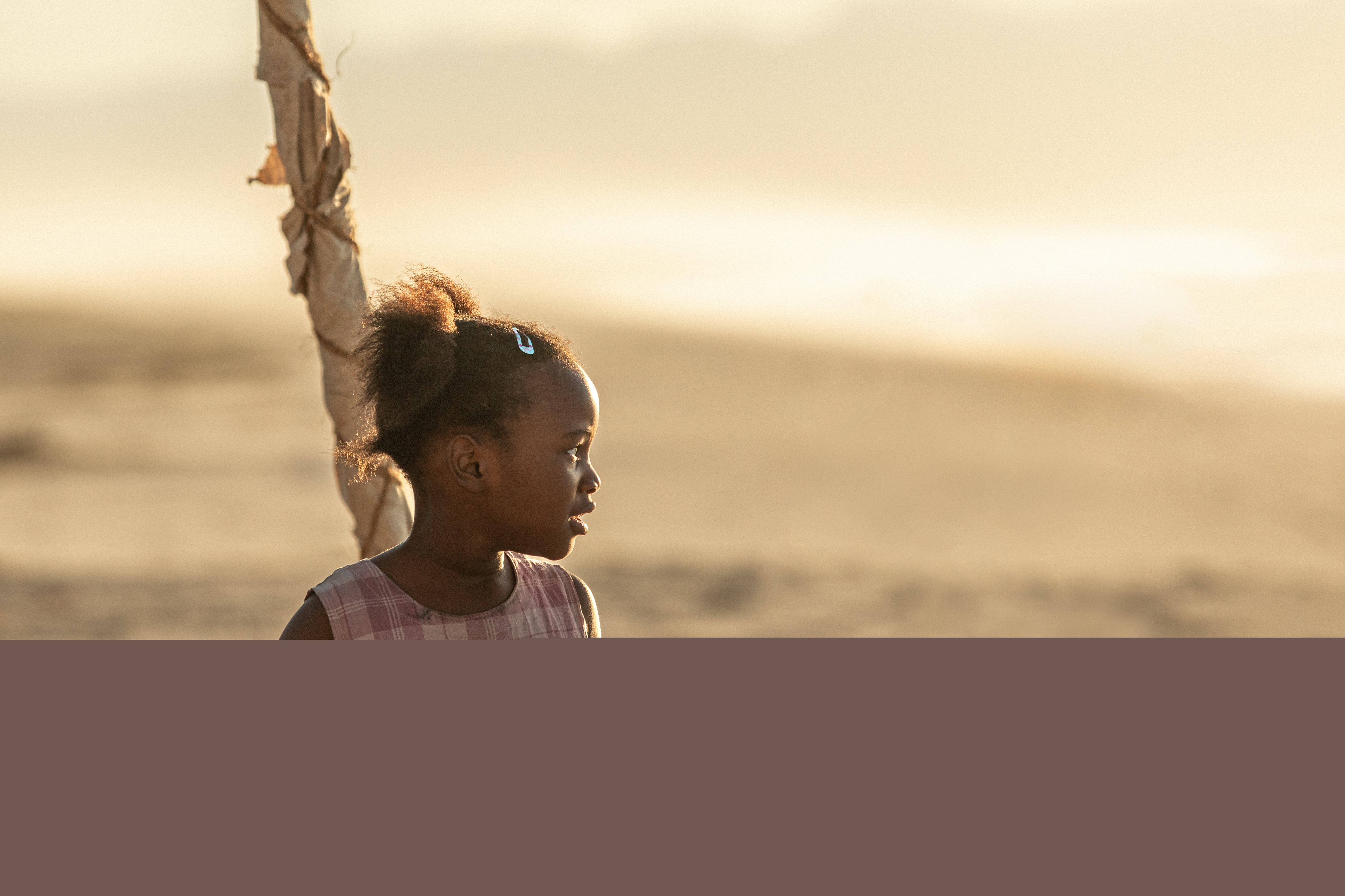 Liten flicka i rosa klänning på en strand i soldengång.