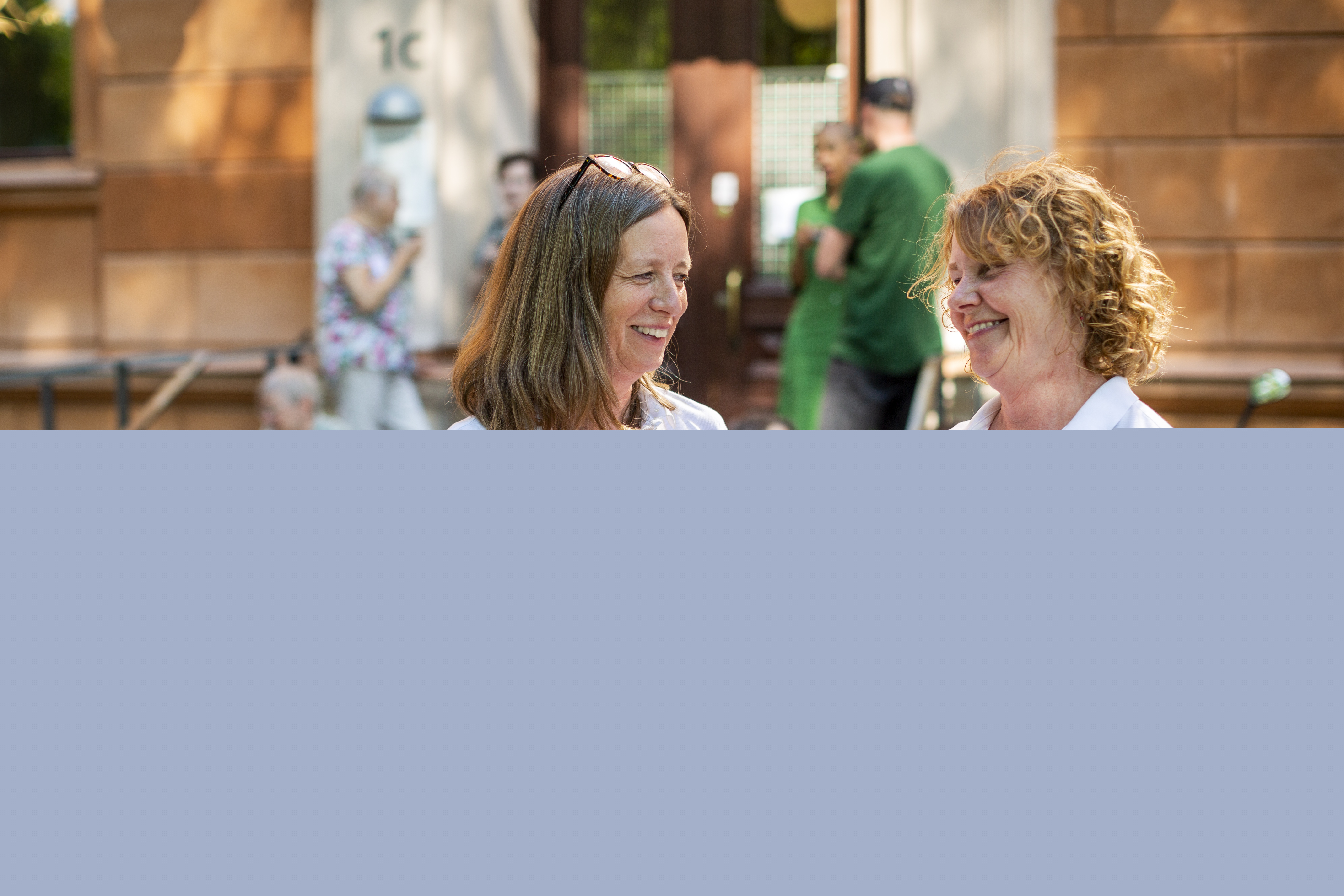 Två kvinnor ler mot varandra. Bakom dem syns fler människor i en trappa.