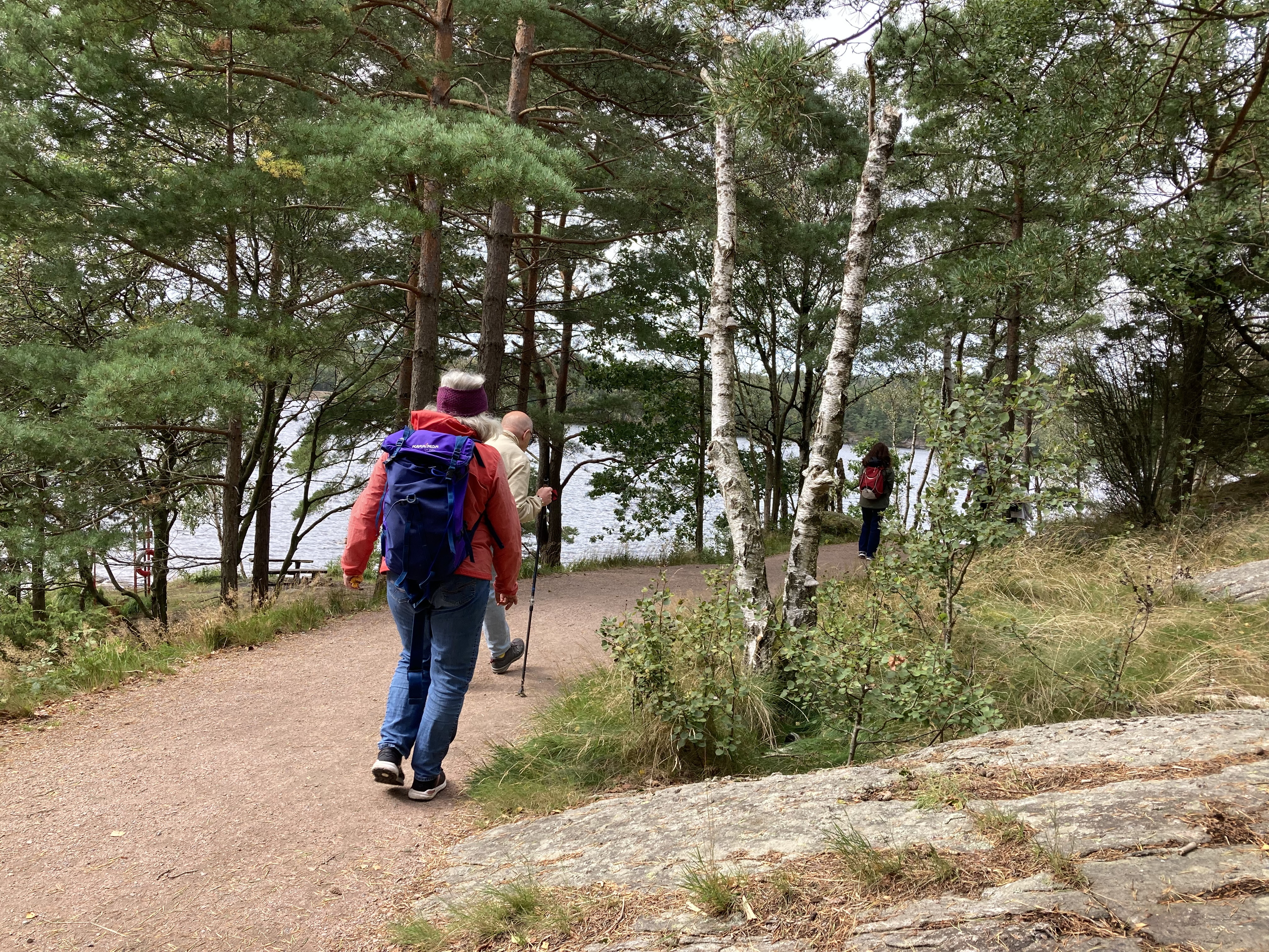 Människor går längs en grusväg vid skog och sjö.