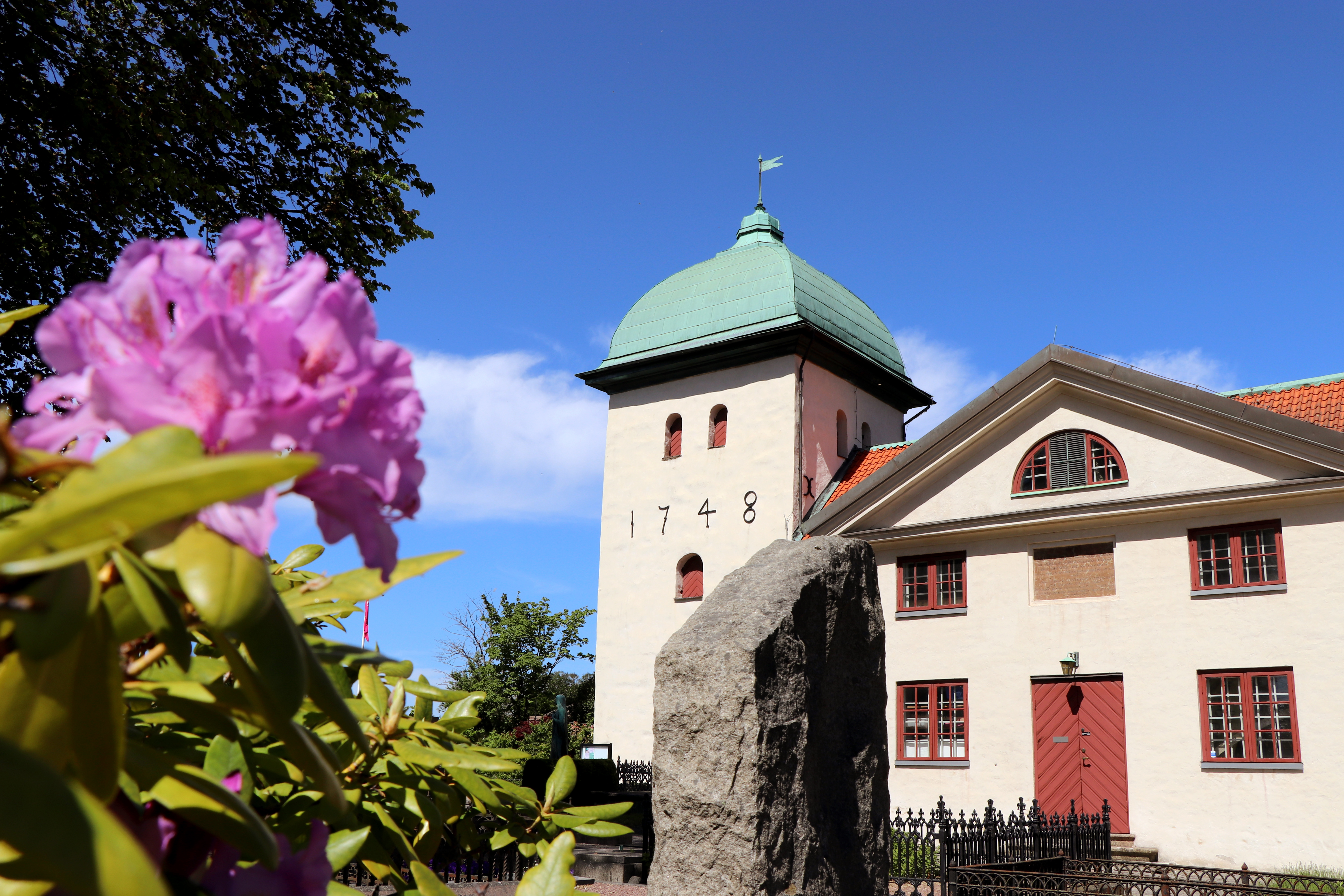 En vit medeltidskyrka omgiven av sommargrönska.