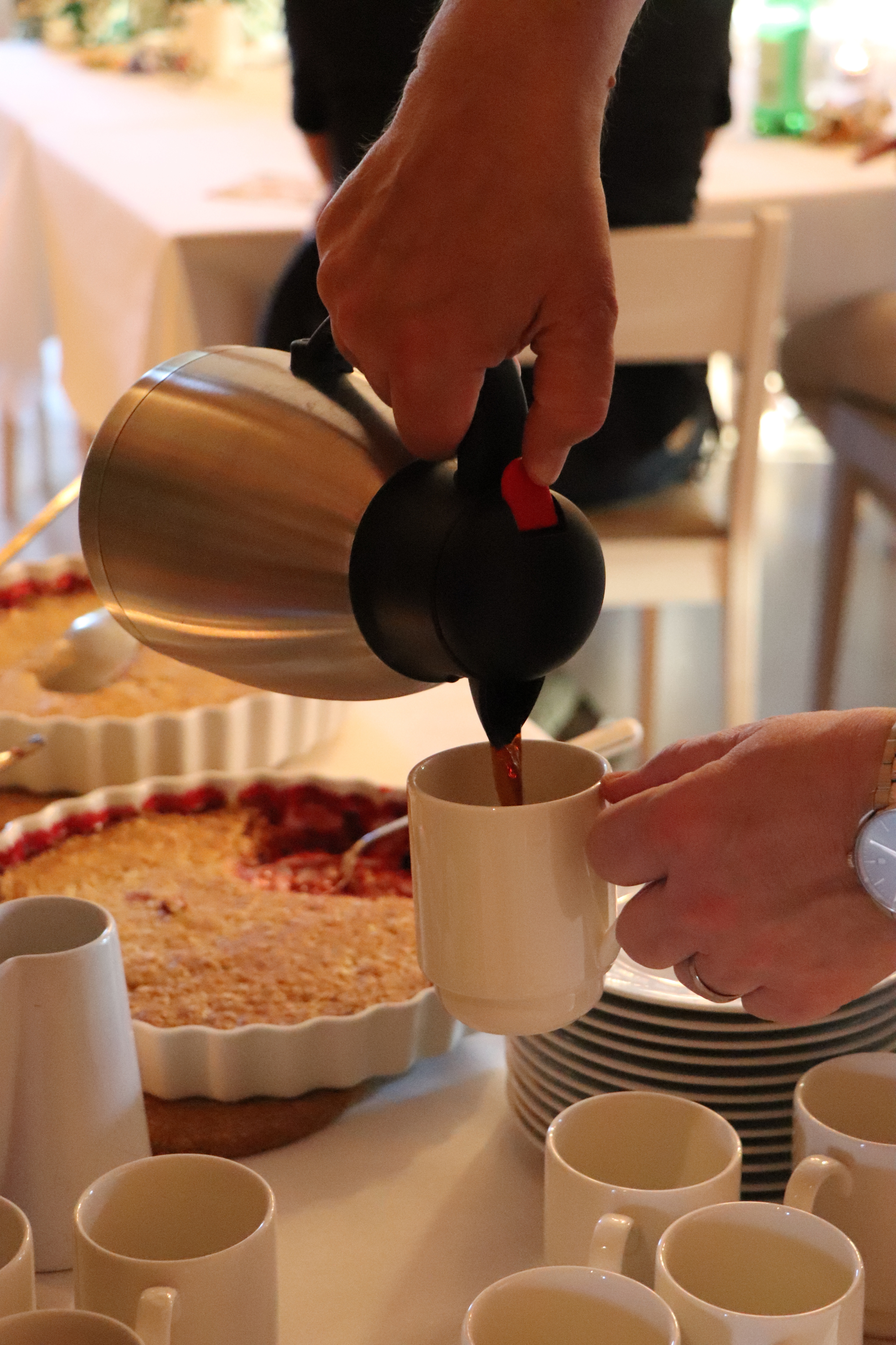 Vita dukar och blommor på borden, kaffe och paj serveras.