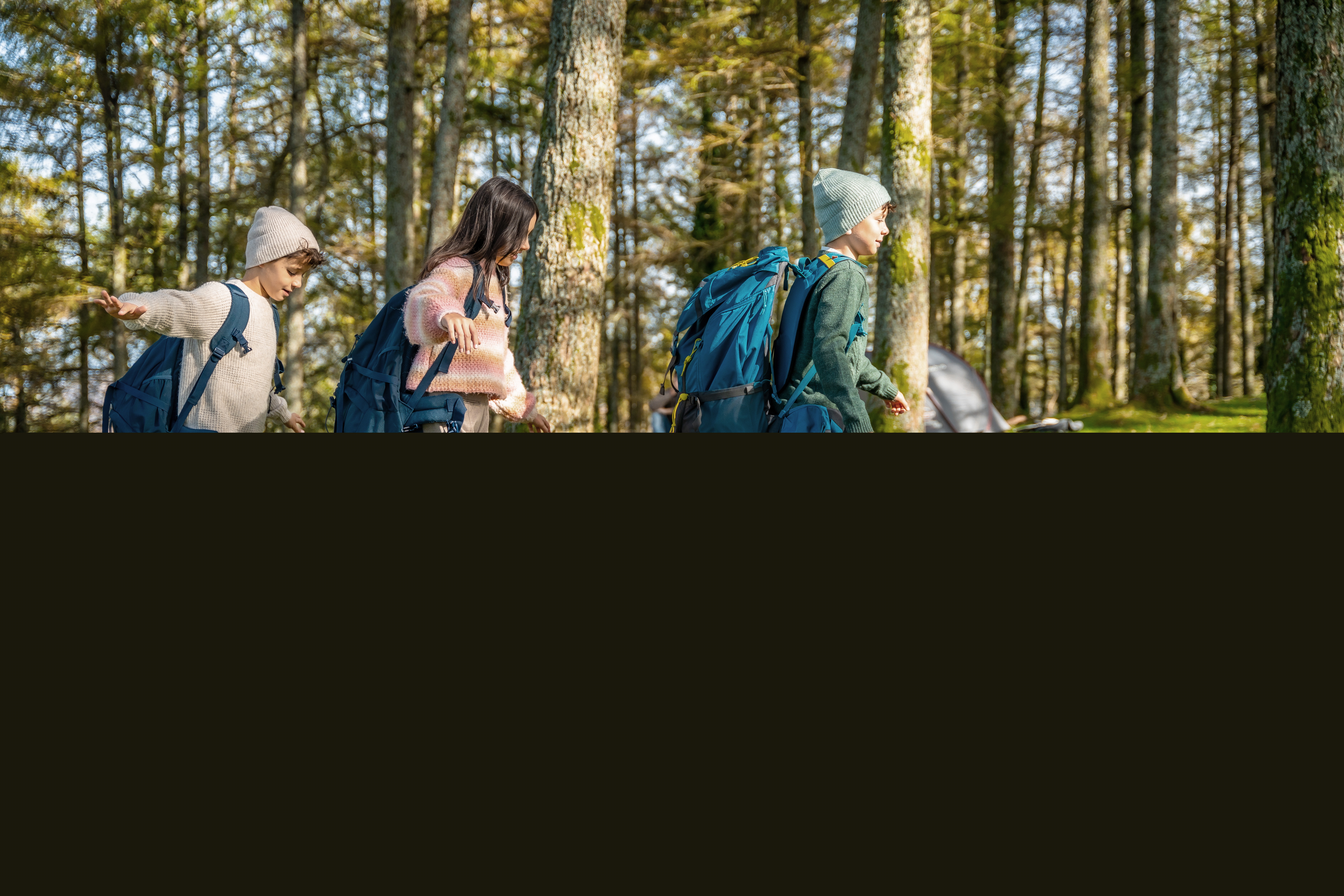 Tre barn balanserar på en fälld trädstam i en grönskande skog.