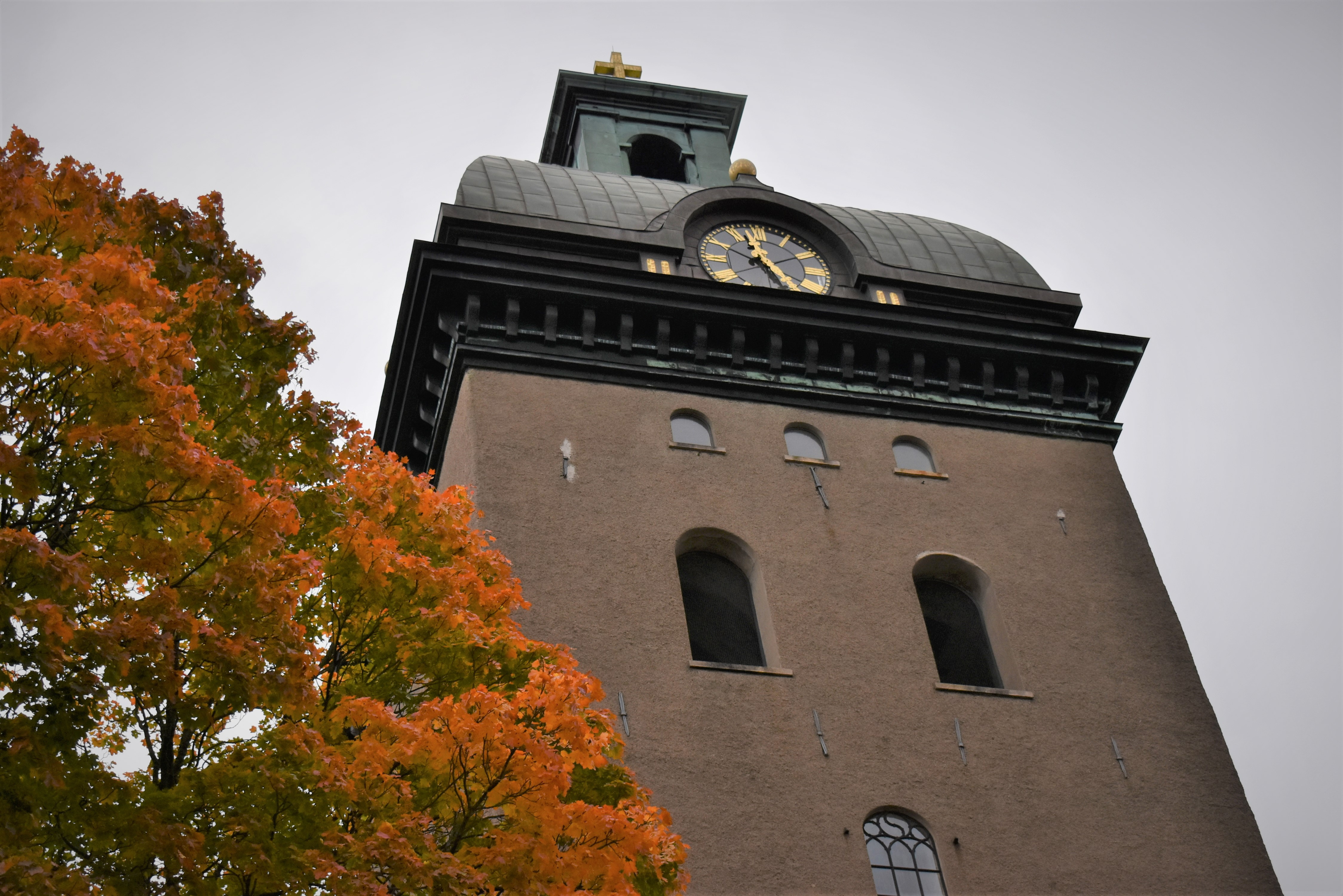 Kyrktorn med höstfärgad trädkrona framför.