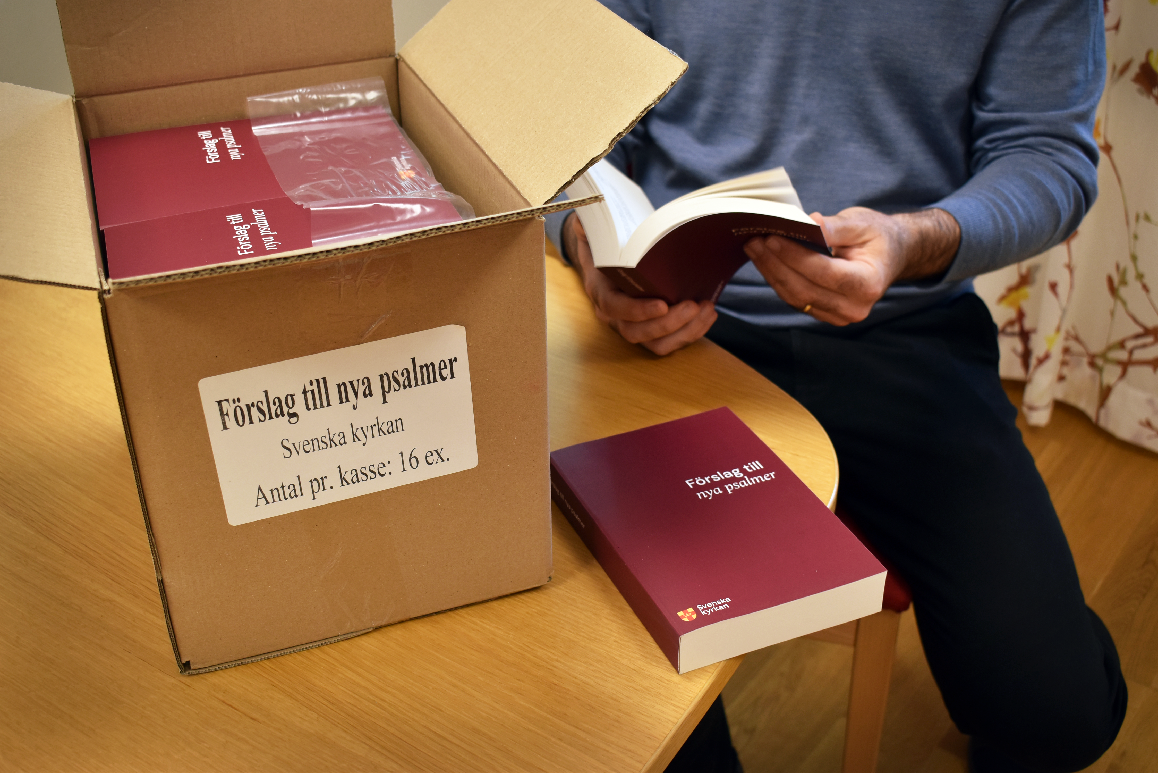 Man bläddrar i psalmbok intill en kartong med psalmböcker.