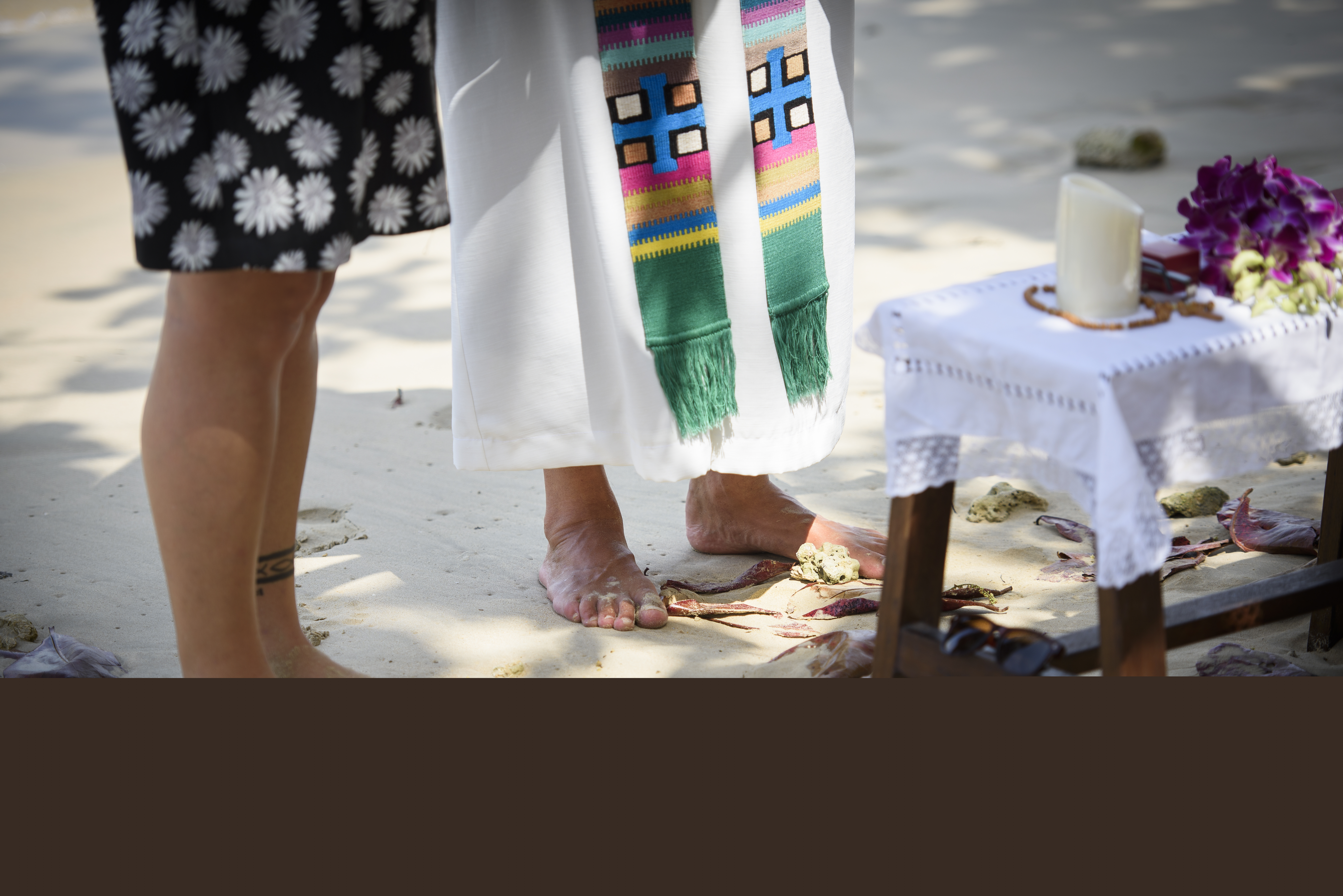 Präst och kvinna står barfota i sanden under en utomhusgudstjänst.