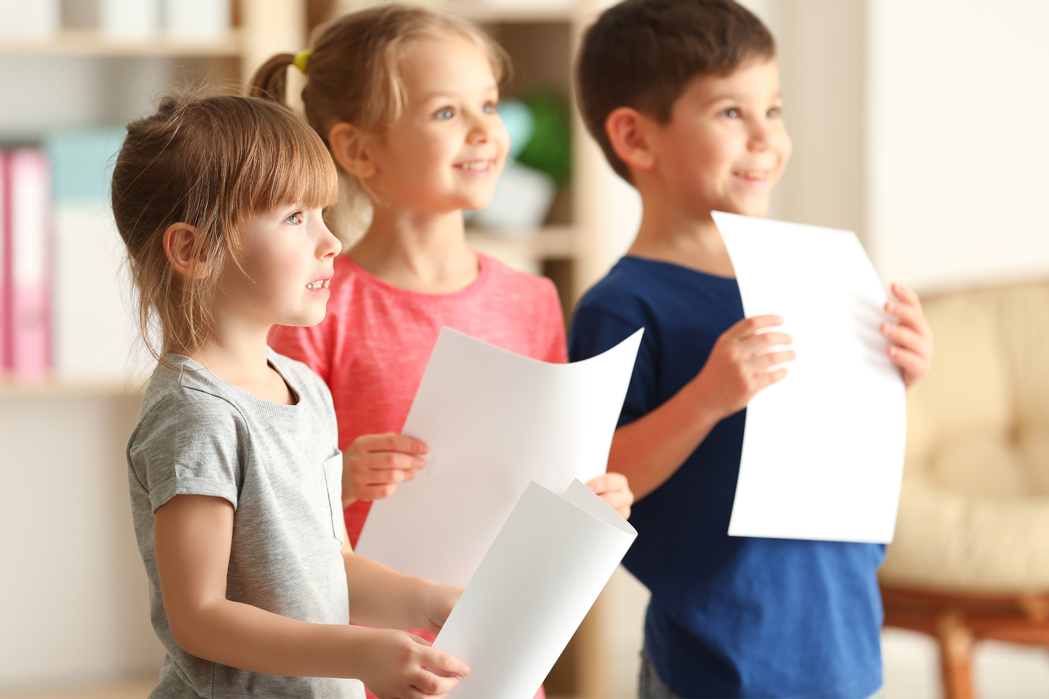 Tre barn står och håller var sitt papper i handen. 