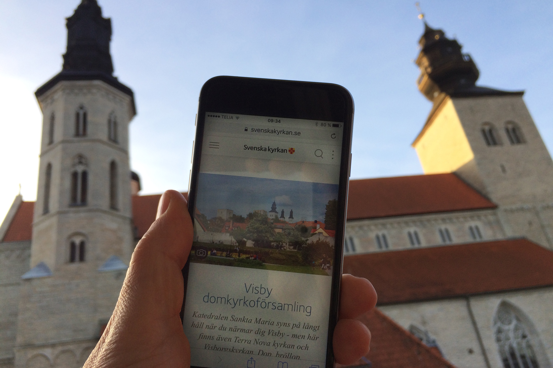 I förgrunden en mobiltelefon som surfat in på församlingens hemsida, i bakgrunden domkyrkan Sankta Maria